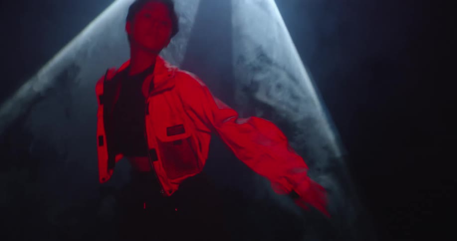 A moving shot of a man posing in a spot under a spotlight