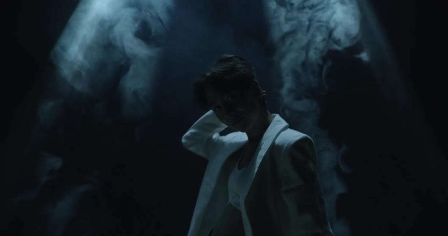 Woman stands under light in dark foggy area