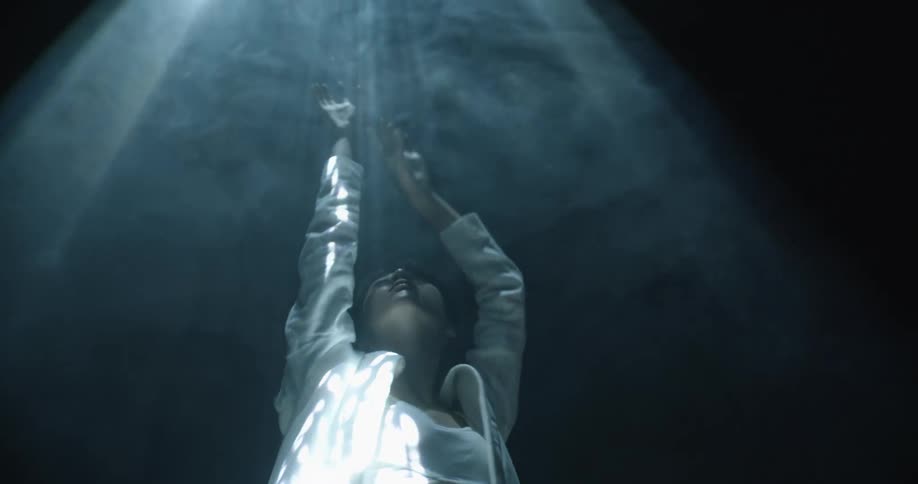 A model poses and dances under a spotlight as smoke floats around her
