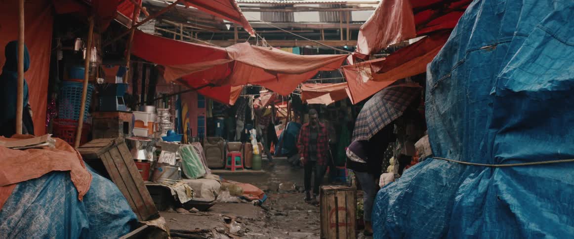 People in a village take shelter under tarps in a outdoor market as rain falls