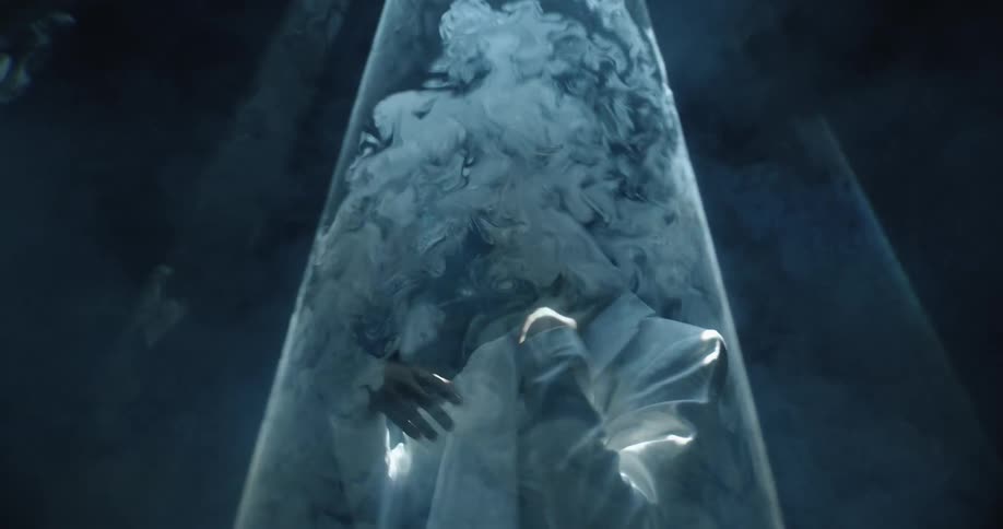Young man wearing a white blazer under strobing lights reflecting in white smoke in a dark room