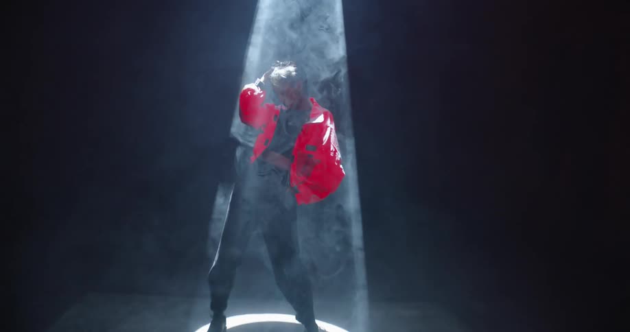 A model poses in a bright orange jacket under a spotlight as fog swirls around her