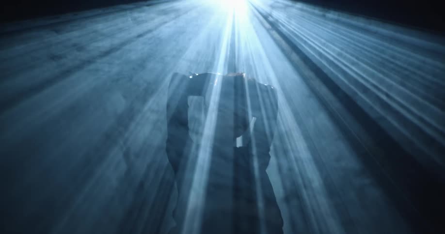 Silhouette of a young man standing in a dark smoky room under strobing spotlight