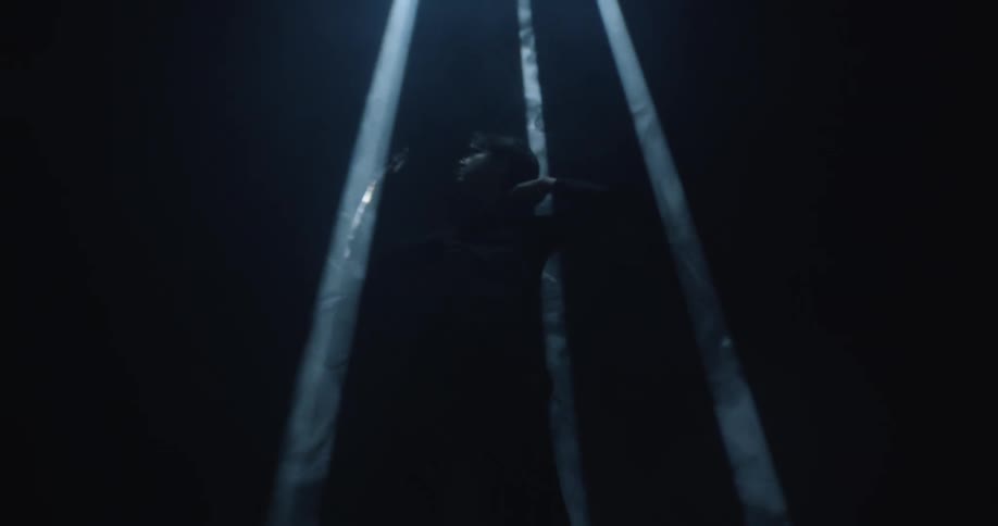 An actress stands under spotlights and raises her arms as if trapped in them