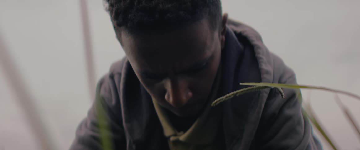 A man is bent down working on the ground outdoors wearing a jacket