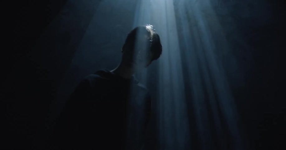 An asian male stands inside in the dark with strobing and flashing lights
