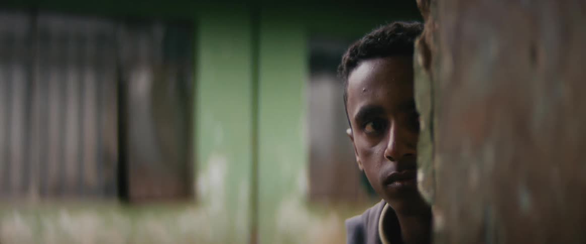 A man is startled walking around a corner outside in front of a building with chipped green paint