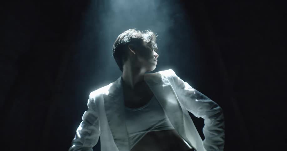 Woman stand under a spot light with smoke all around and poses