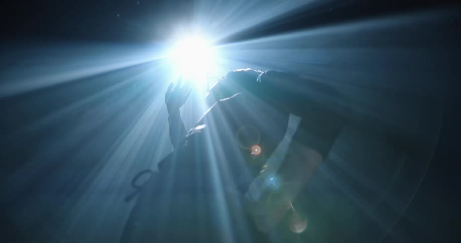 Person under flashing light in a dark room holding up a hand to shield their eyes