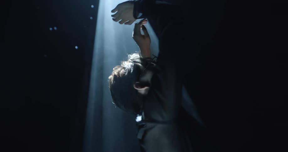 Woman spinning around in a dark room while a beam of light shines down on her