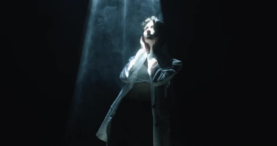 Young man wearing a white blazer under white lights in a dark smoky room