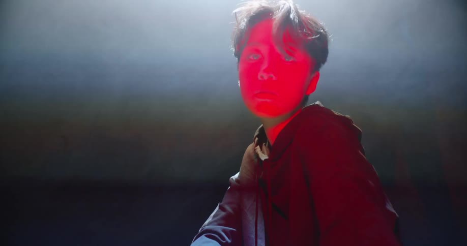 Young man bathed in red light crouching inside a dark smoky room under a strobing spotlight