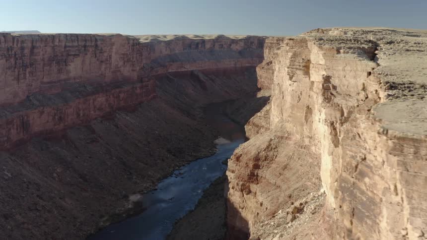 A large canyon with a narrow river running along its floor under a clear daytime sky