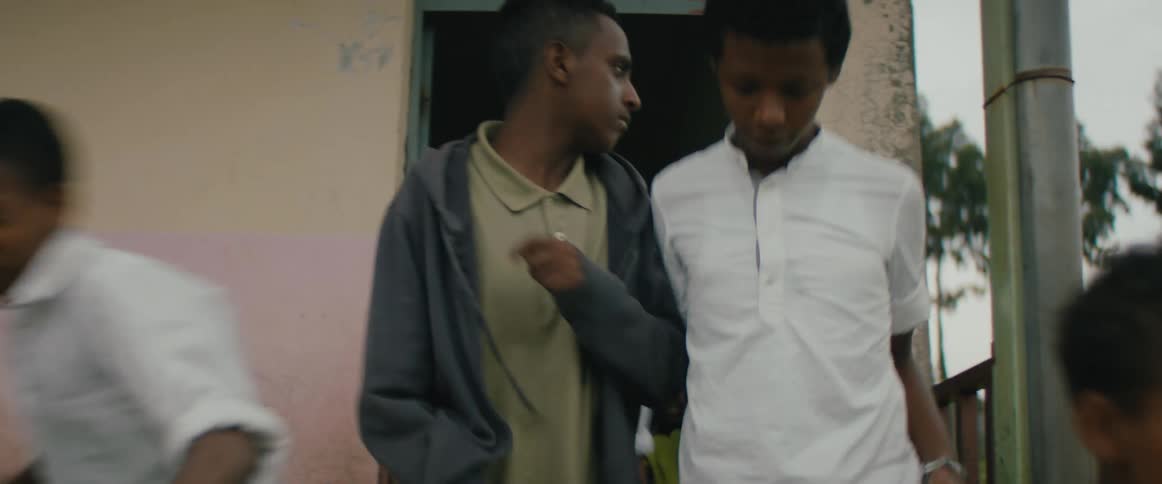 Older boy stands looking around as other boys move out door past him