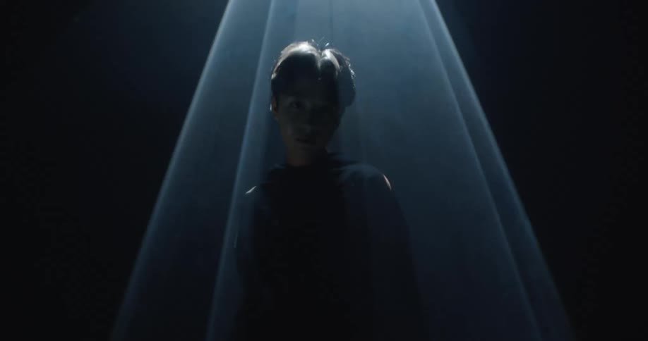 Woman stands and poses under a flashing spotlight with different shapes in a dark room