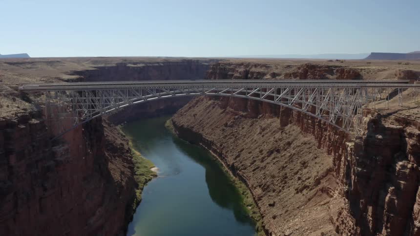 A bridge spanning a canyon containing a calm bluegreen river under a clear blue sky
