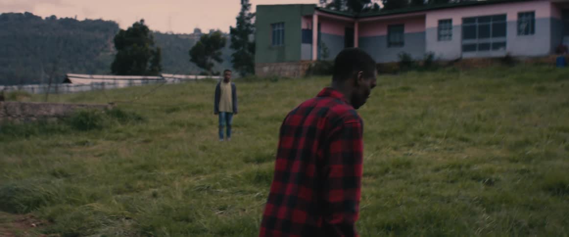 A wounded young man walks across a field while ignoring a concerned boy attempting to talk to him
