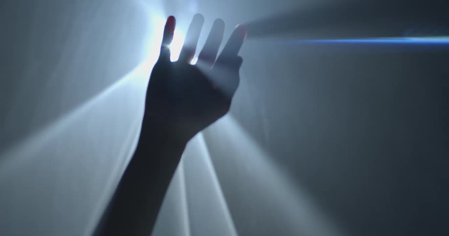 A woman holds her hand up towards a bright light such that only its silhouette can be seen