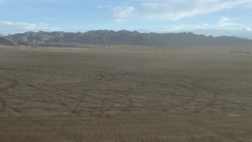 Tire tracks all over ground and mountains on the horizon and a cloudy sky