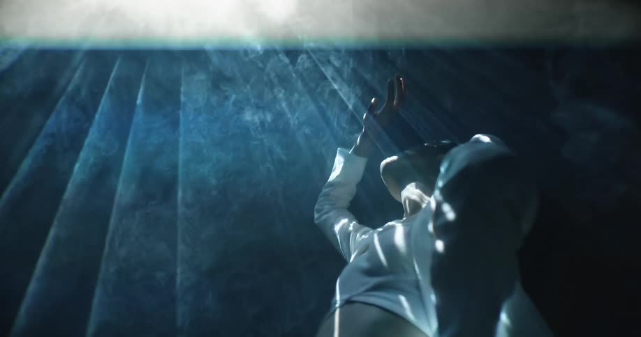 A woman is standing beneath a strobe light with her hand raised above her face