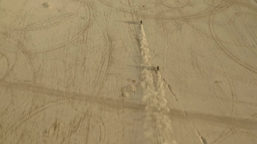 Two motorcycles riding on the dry desert soil leaving trails of dust at evening