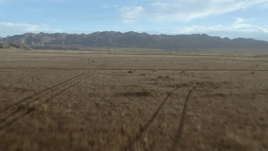 Mountain range across an open field with a few clouds in a blue sky