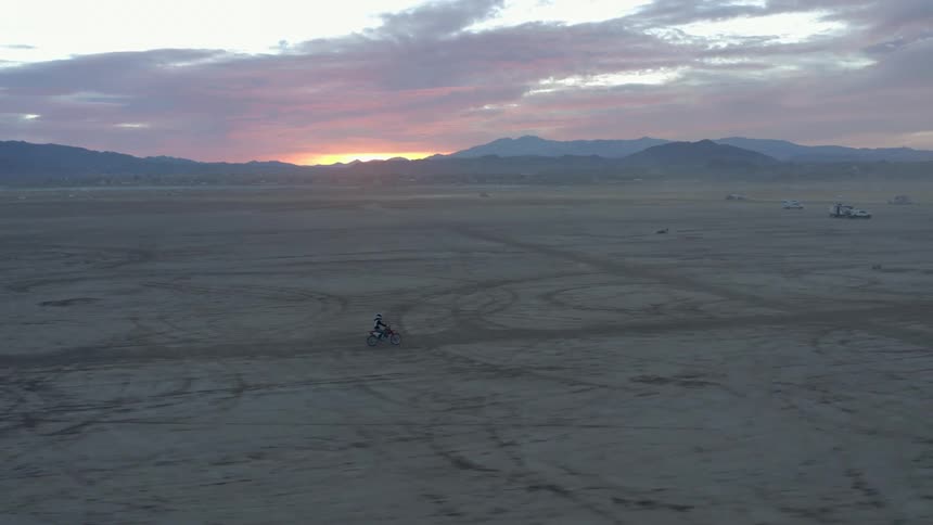 A person drives a motorcycle across a wide open expanse of flat desert