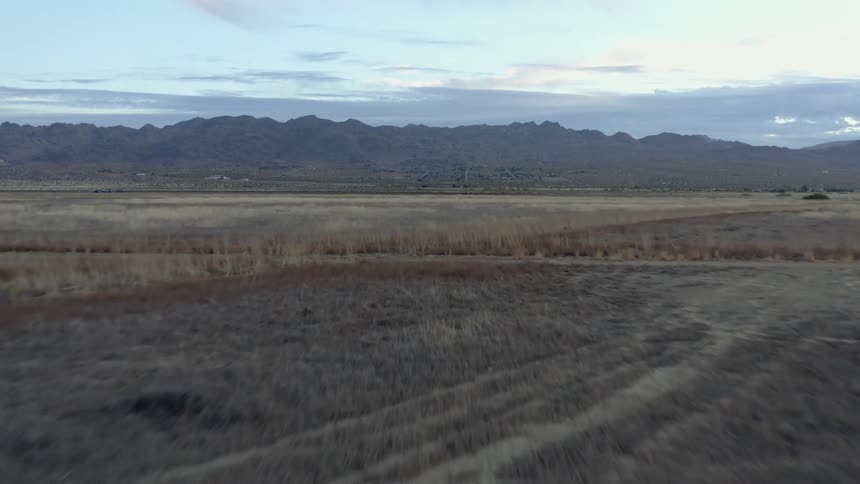 Brown vegetation filled fields stretch to misty mountains crossing road