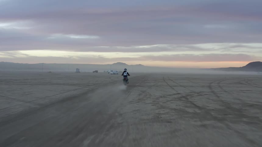 A person rides a motorcyclist offroad across a barren flatland on a cloudy evening