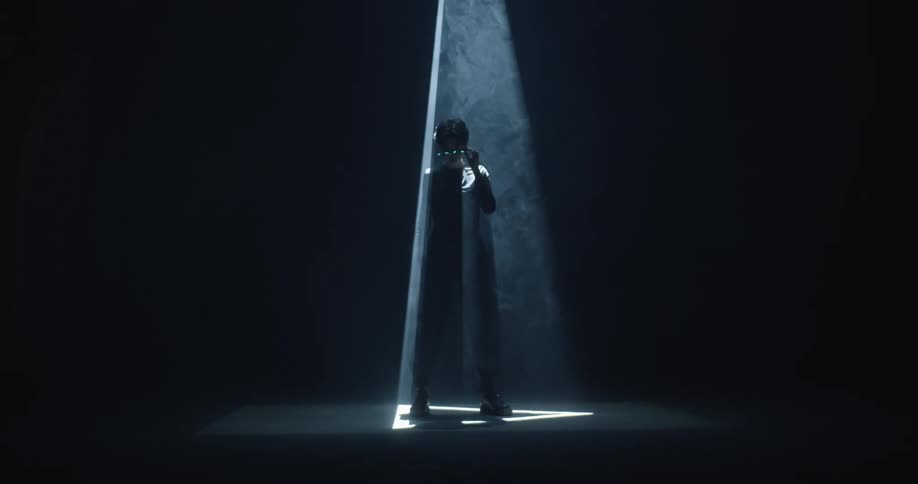 Young man standing in a dark room under the changing strobing lights projecting on the floor