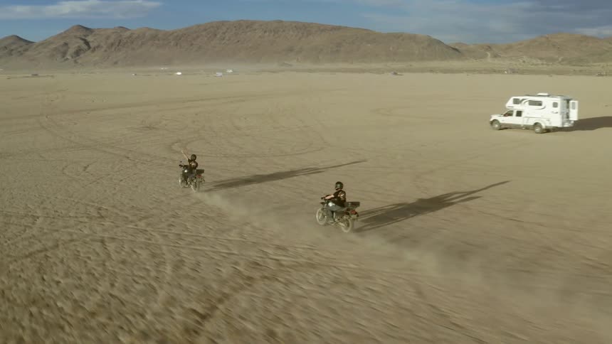 An aerial view of two people riding on motorcycle in the desert during the day