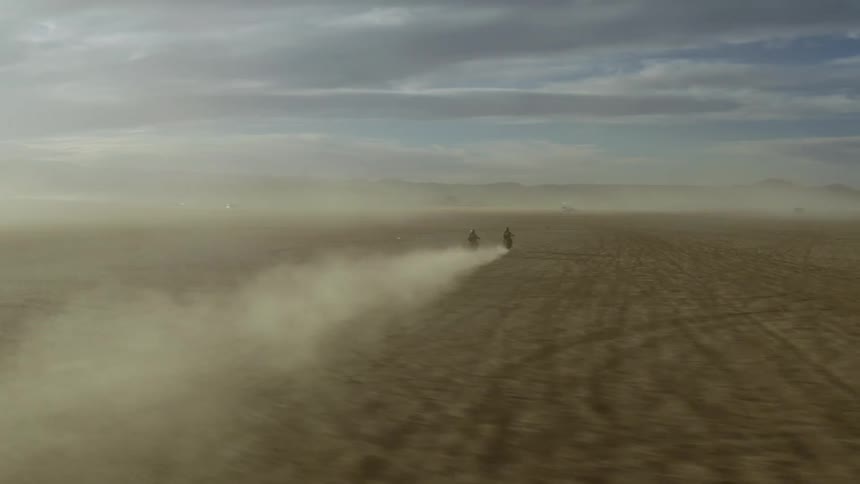 Two people on motorcycles race across a desert