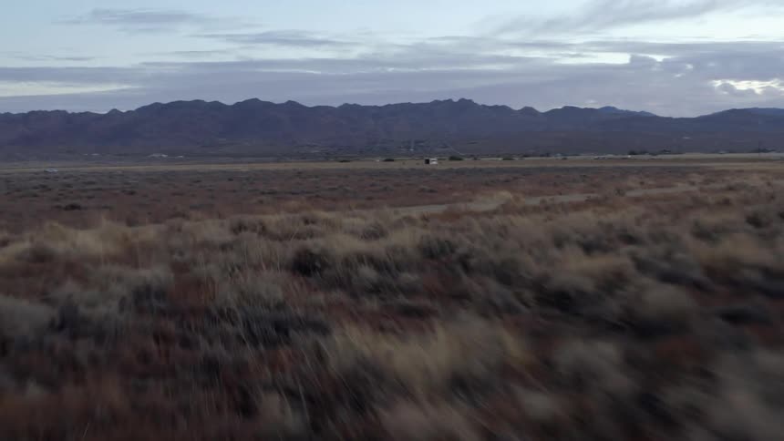 Aerial view of the dry grass on the desert plains near the mountains at sunset