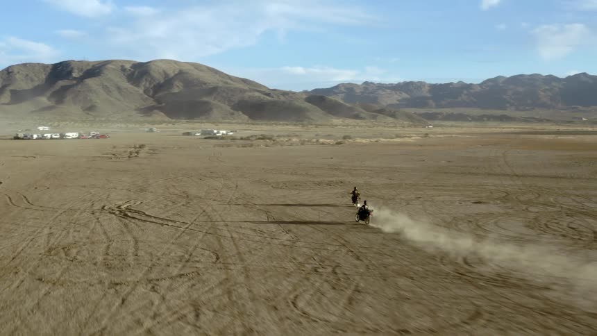 Two people riding motorcycles through a desert with mountains on the horizon