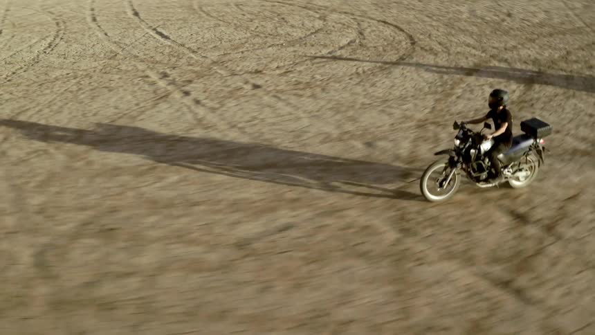 Two motorcycle riders kick up dust as they speed across sand