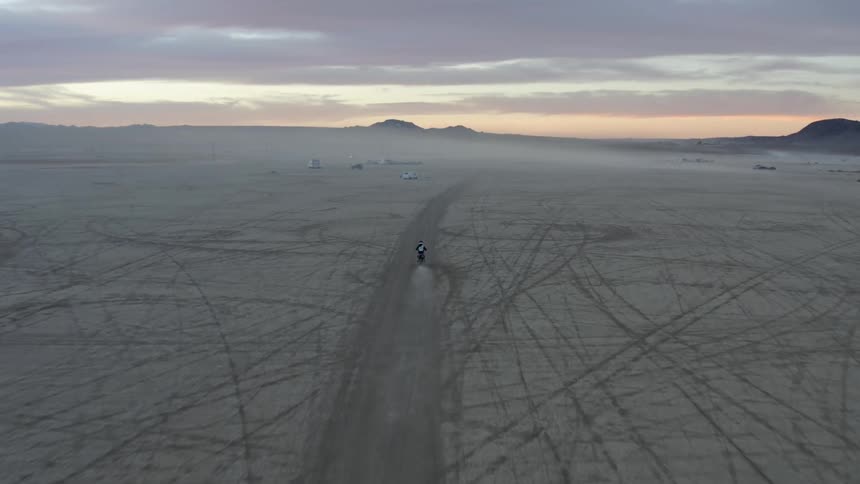 A person sits in their truck and watches a motorcycle drive across a desert
