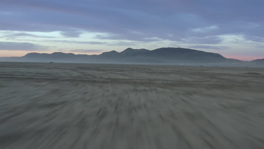 Ground covered in tire tracks with fog and mountains on the horizon and a cloudy sky