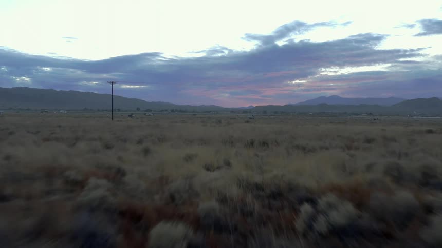 The camera quickly flies above wide open grasslands under a cloudy sky