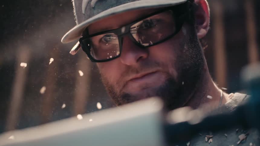 A man wearing glasses is shaving wood