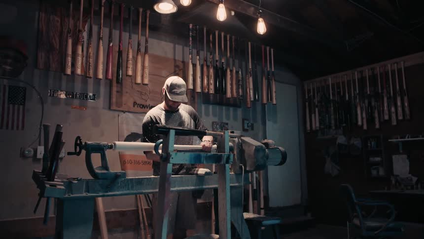 Man fabricating a baseball bat on a machine in a shop