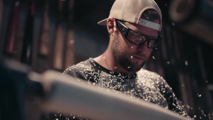 Sawdust flies up around a man working on a piece of wood
