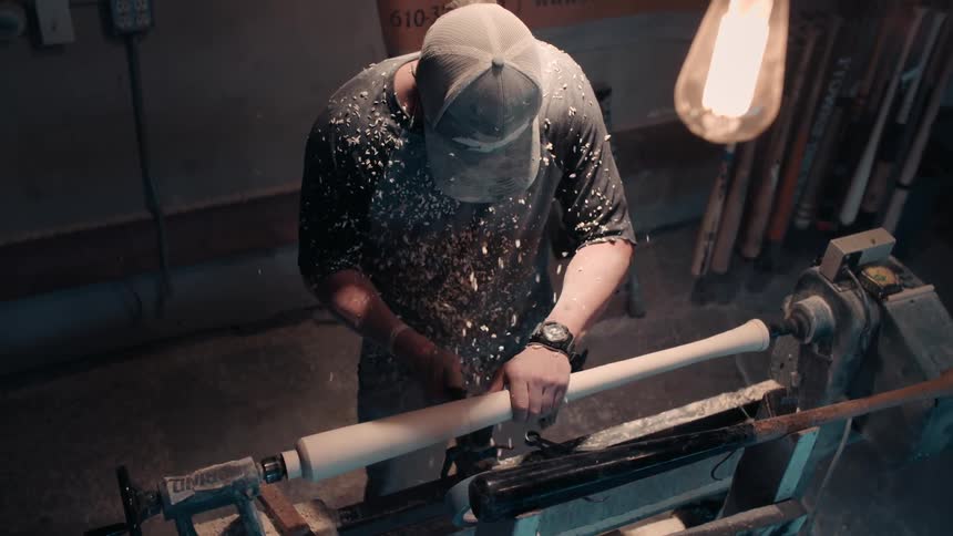 A man is carving a baseball bat in a shop