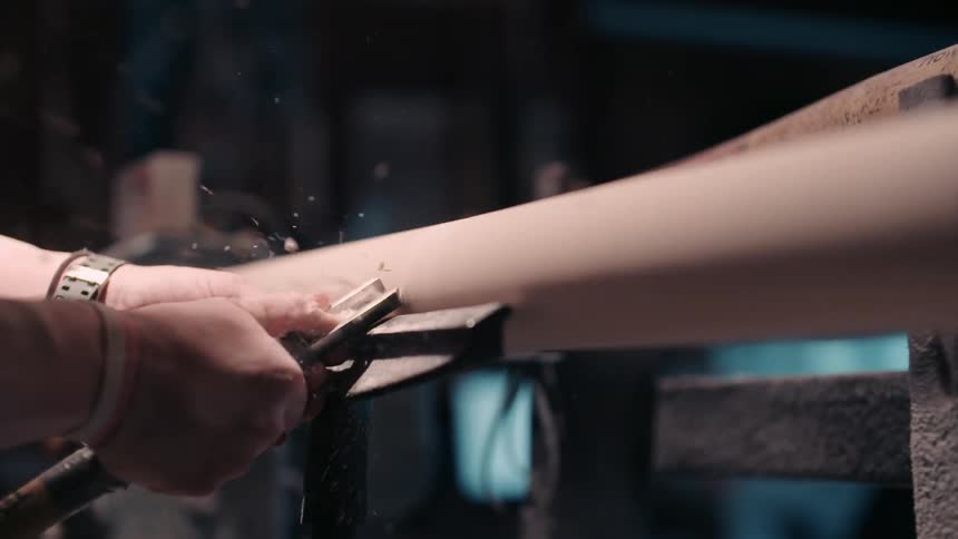 A person shaves a long wooden pole