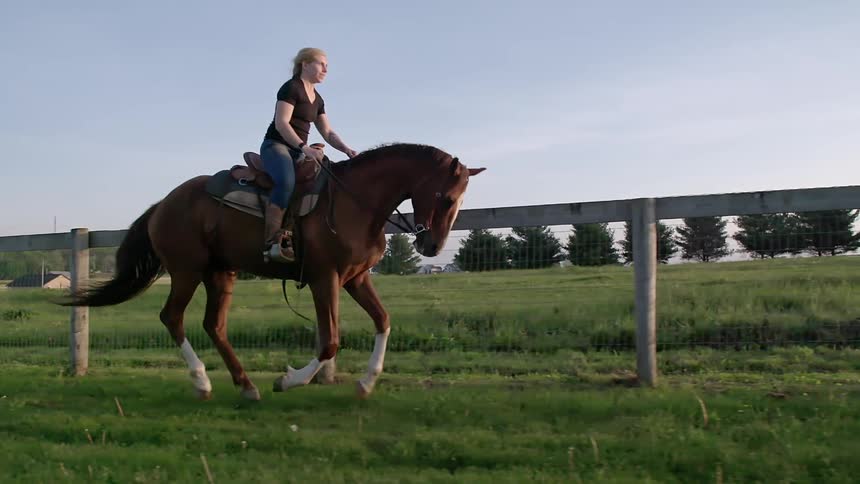 A woman rides a horse in a rural area