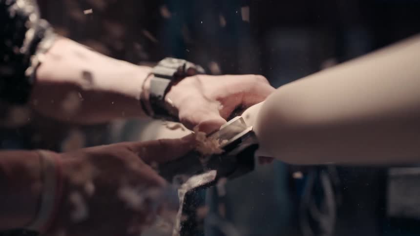 A man's hands use a wood awl to carve a piece of wood