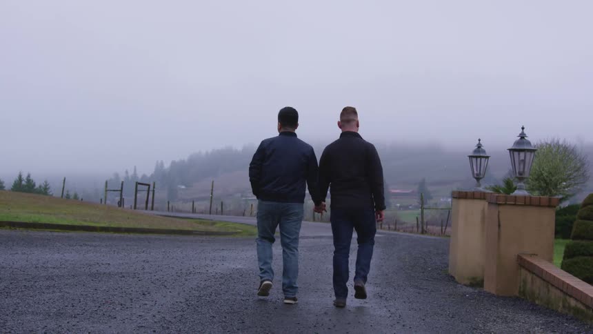 Two men hold hands as they take a walk together along a gravel covered road on an overcast day