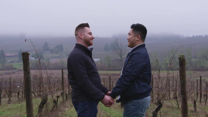 Two men are holding hands outdoors in a rural area