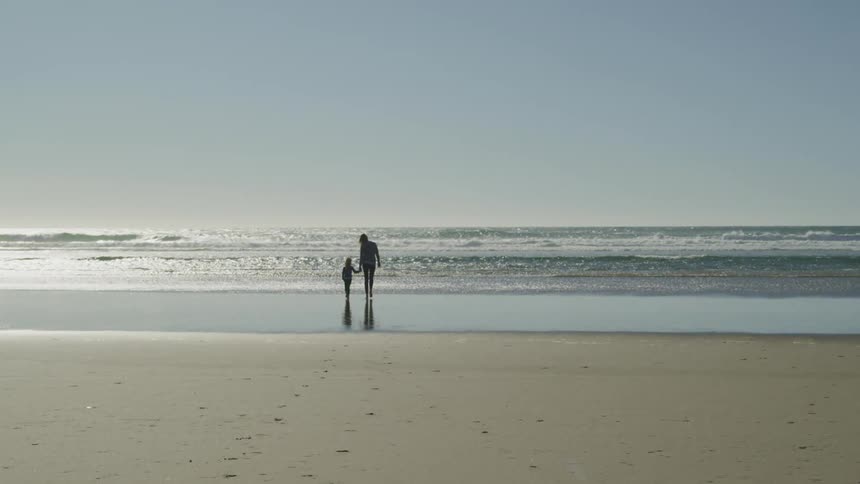 Two people walk on the beach by the water