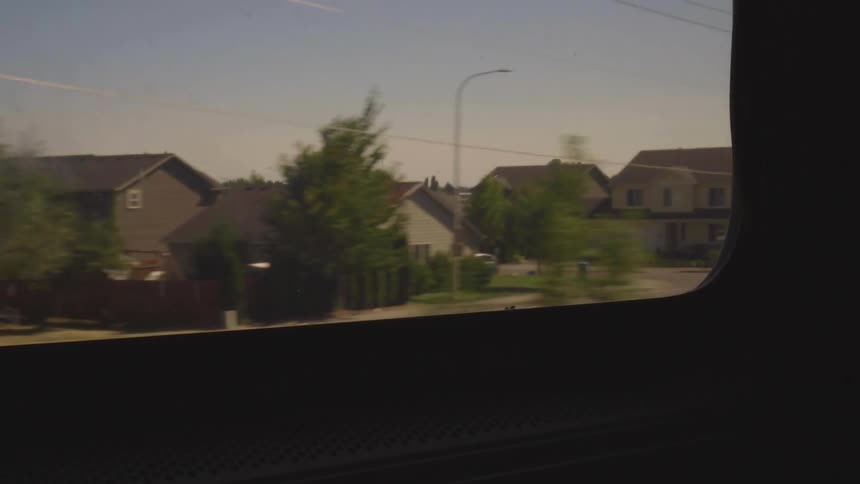A vehicle passes by a neighborhood that is surrounded by farmland