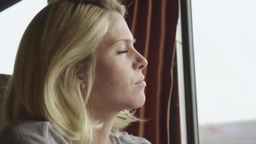 A woman sits in a vehicle and stares out the window as objects pass by it